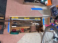 Wooden box filled with various hand tools such as a wooden mallet, hammer, bolt cutters, yellow level, and more; some tools lean against the box showing signs of rust and use.