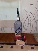 Full view of Oreck upright vacuum cleaner with vacuum bags and red vacuum accessories around the base.