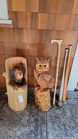 Wood carvings of a bear and an owl, wooden cane, and two wooden baseball bats placed upright against a wall.