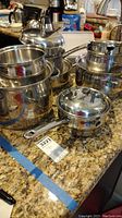 Full set of Belgique stainless steel cookware including pots, pans, and lids on a granite countertop.