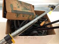 Photo of a cardboard box filled with various clamps including metal bar clamps with yellow plastic handles.