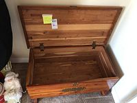 Open wooden chest showing cedar wood lining inside, brass hinges, and front brass decorative hardware plate.