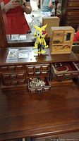 Photo showing wooden dresser top with open drawers containing costume jewelry, yellow earring holder, and wooden jewelry box.