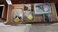 Drawer of costume jewelry containing several clear plastic containers and bags with bracelets, necklaces, earrings.