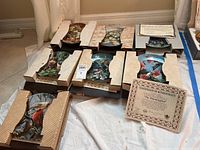 Seven decorative wall plates in original packaging laid out on floor with certificates included.