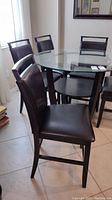 Five dark wooden dining chairs with black faux leather seats and backs around a glass-top table.