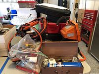 Photo showing the overall collection including jumper cables, battery charger, plastic organizer boxes, and a metal case with butane propane cylinder inside.