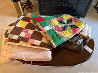 Overview of 3 hand sewn quilts and 3 throw blankets stacked on a wooden table.