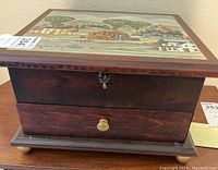 Closed wooden jewelry box with scenic village painting on the lid, showing front and side panel detail.