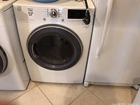 Front view of white Kenmore electric dryer, visible control panel, circular door closed, showing dryer from a slight angle.