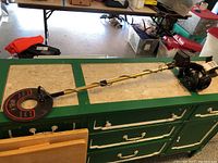 Full metal detector with extended shaft, hand grip, control box, and headphones placed on countertop.