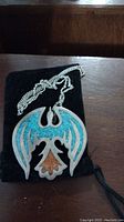 Phoenix pendant necklace with turquoise and coral inlay on silver chain against black background.
