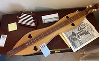 Mountain dulcimer and xylophone placed atop a surface with dulcimer music books underneath, showing dulcimer's wooden body and the heart-shaped sound holes.