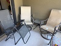 View of two metal swivel rocking chairs with beige fabric, folded black reclining chair, and small glass top table on an outdoor patio.