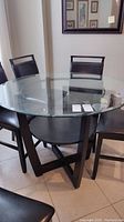 Overview of the round glass top dining table with wooden base and chairs around it