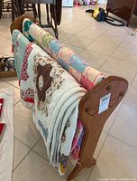 Wooden quilt stand holding three hand sewn quilts draped over it in a tiled room.
