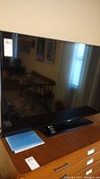 Samsung television on wooden dresser showing the front and screen reflective surface
