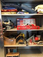 Four metal shelves filled with folded moving blankets and workshop tools including a router, mitre saw accessories and various cables.