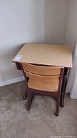 School desk and chair set placed against wall on carpeted floor, showing wooden surfaces and metal legs.