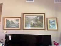 Three framed Paul Sawyer signed and numbered landscape prints hung above a television, the largest print centered with two smaller prints on each side.