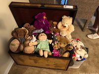 Open trunk showing a variety of stuffed animals and dolls including a Cabbage Patch doll and several teddy bears