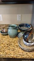 Thirteen pieces of vintage pottery in various shapes and glazes arranged on a kitchen countertop.