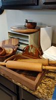 View of wooden rolling pins, wooden salad bowl, wooden trivets, and part of paper towel holder on kitchen counter