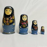 Front view of four Russian nesting dolls with black scarves and blue dresses decorated with flowers placed in size order