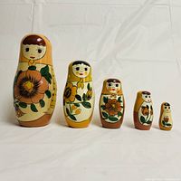 Front view of five flower-themed Russian Matryoshka nesting dolls in descending size order, showing hand-painted floral and face designs.