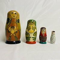 Front view of four nesting dolls including a person holding a frog, green frog, and two smaller human-like figures