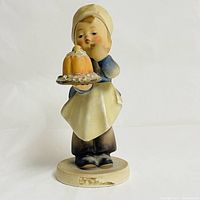 Front view of the Goebel Hummel baker figurine holding a cake with visible chip on the base front