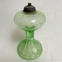 Front view of the green Depression glass oil lamp showing the fluted base and rounded reservoir top with metal burner holder.