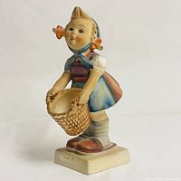 Side view of Goebel Hummel Little Helper figurine showing colorful illustration and detail of basket