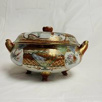 Side angle showing the detailed floral, geometric and figurative Nippon Imari design on the covered porcelain bowl with gold accents and feet.
