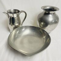 A group photo of the three pewter items including a round vase, shallow bowl and a pitcher showing the whole collection.