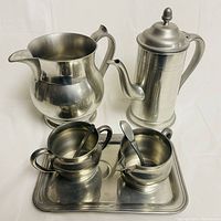 Overall view of the pewter set showing all 5 pieces including pitcher, coffee pot with lid, creamer, sugar bowl with spoon, and tray