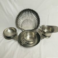 Front angle showing five pewter serving pieces including shell tray, two handled dishes, pitcher and bowl.