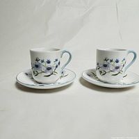 Photo showing both Shelley teacups and saucers side by side on a plain background, displaying floral pattern and light blue handles.