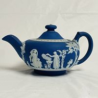 Side view of the Wedgwood blue jasperware teapot showing the classical white relief designs of figures and trees.