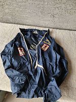 Blue vintage jacket laid flat to show front, collar, and overall condition with visible patches and zipper detail.
