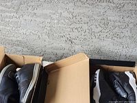 Top-down view of two pairs of sneakers in their respective open shoe boxes, showing condition and partial size labels.