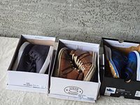 Three pairs of men's sneakers displayed in original boxes against a concrete background.