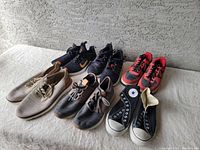 Six pairs of men's shoes arranged in two rows on a gray carpeted surface, including athletic sneakers, casual shoes, and Converse sneakers