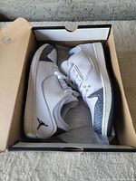 Pair of white and gray Air Jordan 1 Low sneakers placed inside a cardboard shoe box with visible wear. The shoes have elephant print detail and Nike Air Jordan logos.