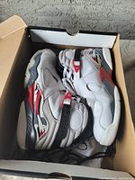Pair of white Air Jordan high-top basketball sneakers with red, black, and gray accents in original box.