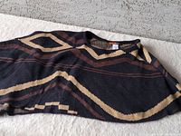 Flat lay of knit shawl displaying abstract geometric patterns in black, tan, and brown tones on a knit fabric with round neckline.