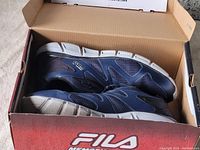 Pair of navy blue Fila sneakers inside original Fila branded cardboard box shown partially open