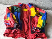 Front view of vintage colorful leather jacket showing patchwork design in red, blue, yellow, green and black leather panels. Elastic cuffs and gathered waist visible.