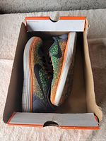 Nike sneakers inside original box showing lateral side and sole base in multicolor green, orange, and black pattern with white midsole.