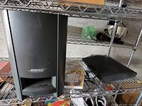 Bose Acoustimass speaker subwoofer and PS3 console on metal shelves with game case
